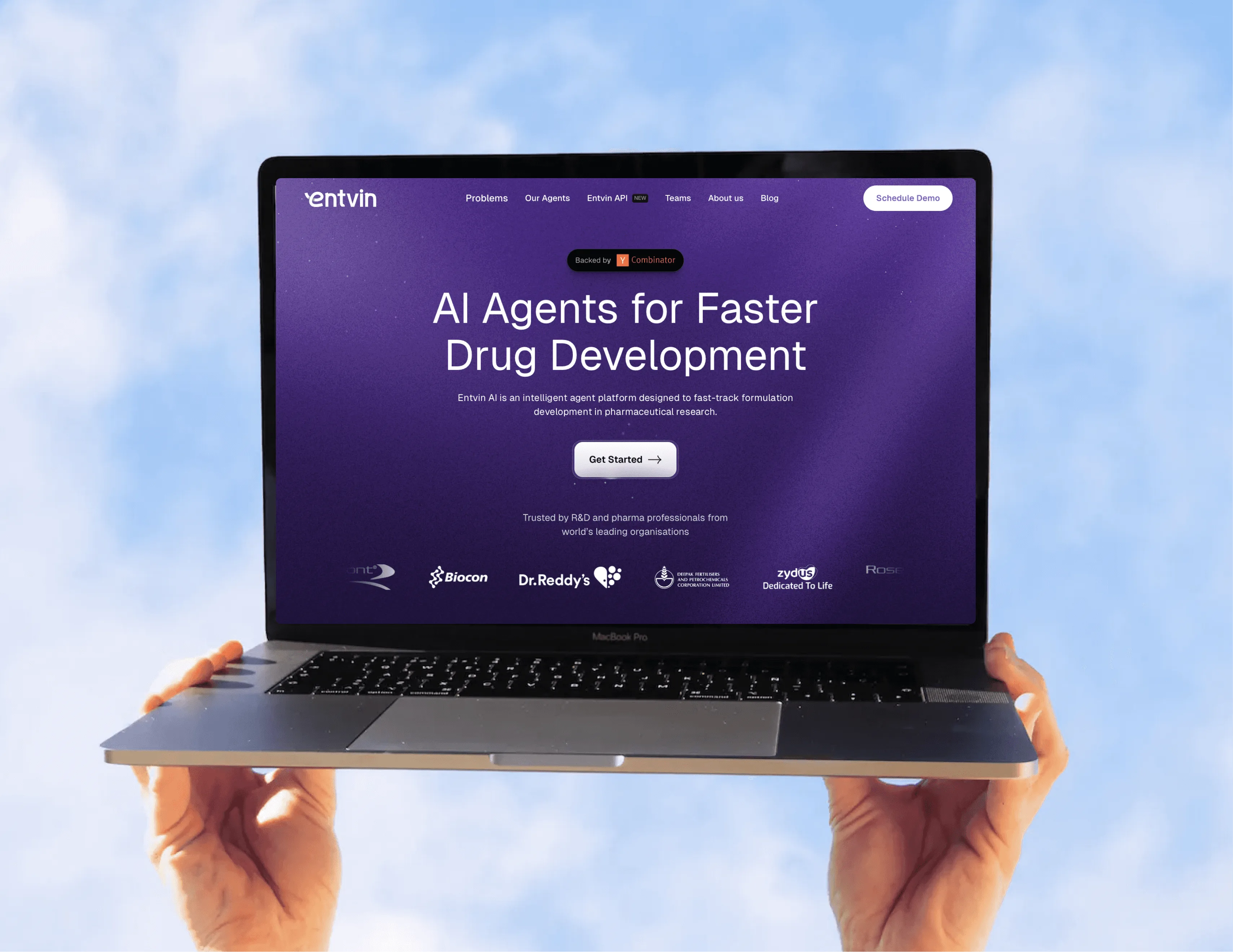 Entvin website hero 'AI Agents for Faster Drug Development' with a Get Started button and pharma customer logos including Biocon and Dr. Reddy's, on a laptop held up against the sky
