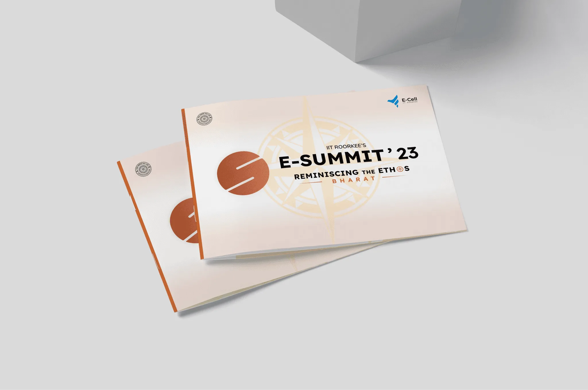 Two wide sponsorship deck covers with the copper E-Summit '23 logo and a faint compass on cream, on a grey surface